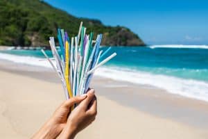 Used plastic straws held in a hand on a beach - we are aiming to be more environmentally sustainable
